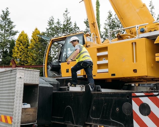 Certified crane operator getting in a mobile crane. Operator climbing on Construction crane lifting heavy freight. Modern mobile transportation technologies help building house. Real estate professional company working with big machines. Close-up